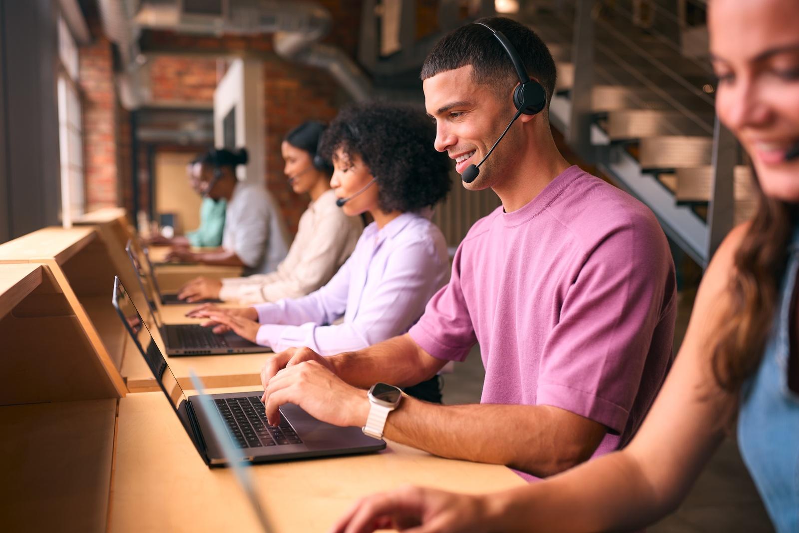 People wearing headsets working on laptops in a row at a long desk