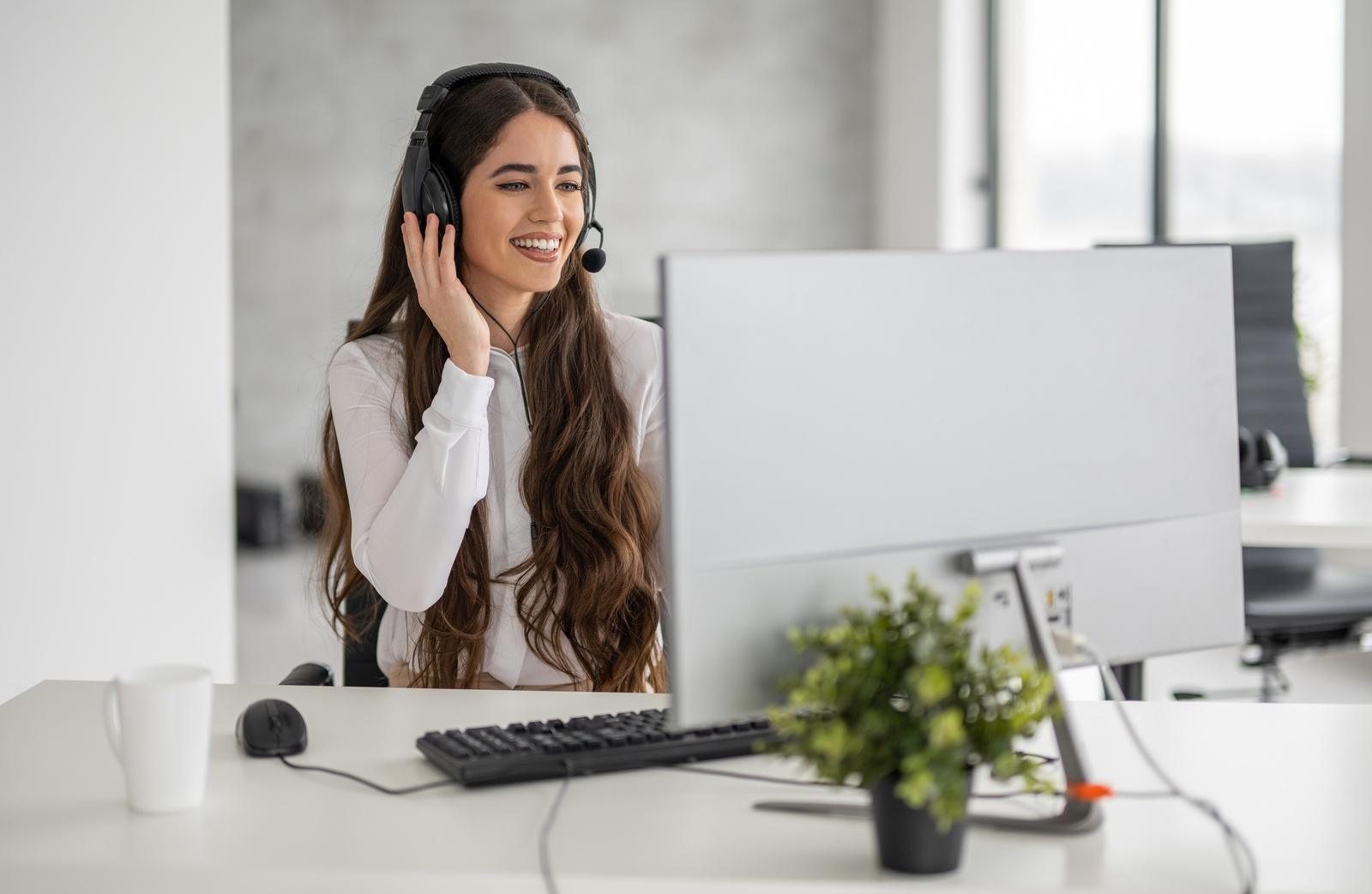Smiling person wearing a headset at a desk in front of a computer monitor